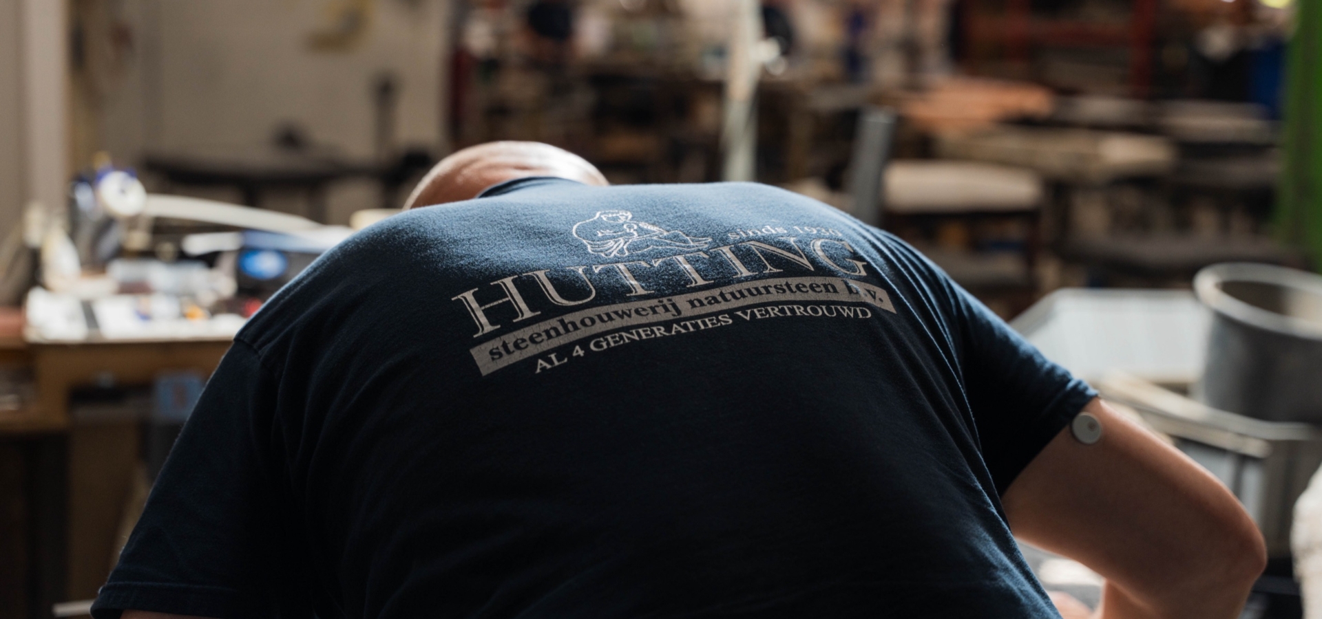 Vakman in de werkplaats met het Hutting-logo op zijn rug: steenhouwerij natuursteen, al 4 generaties vertrouwd
